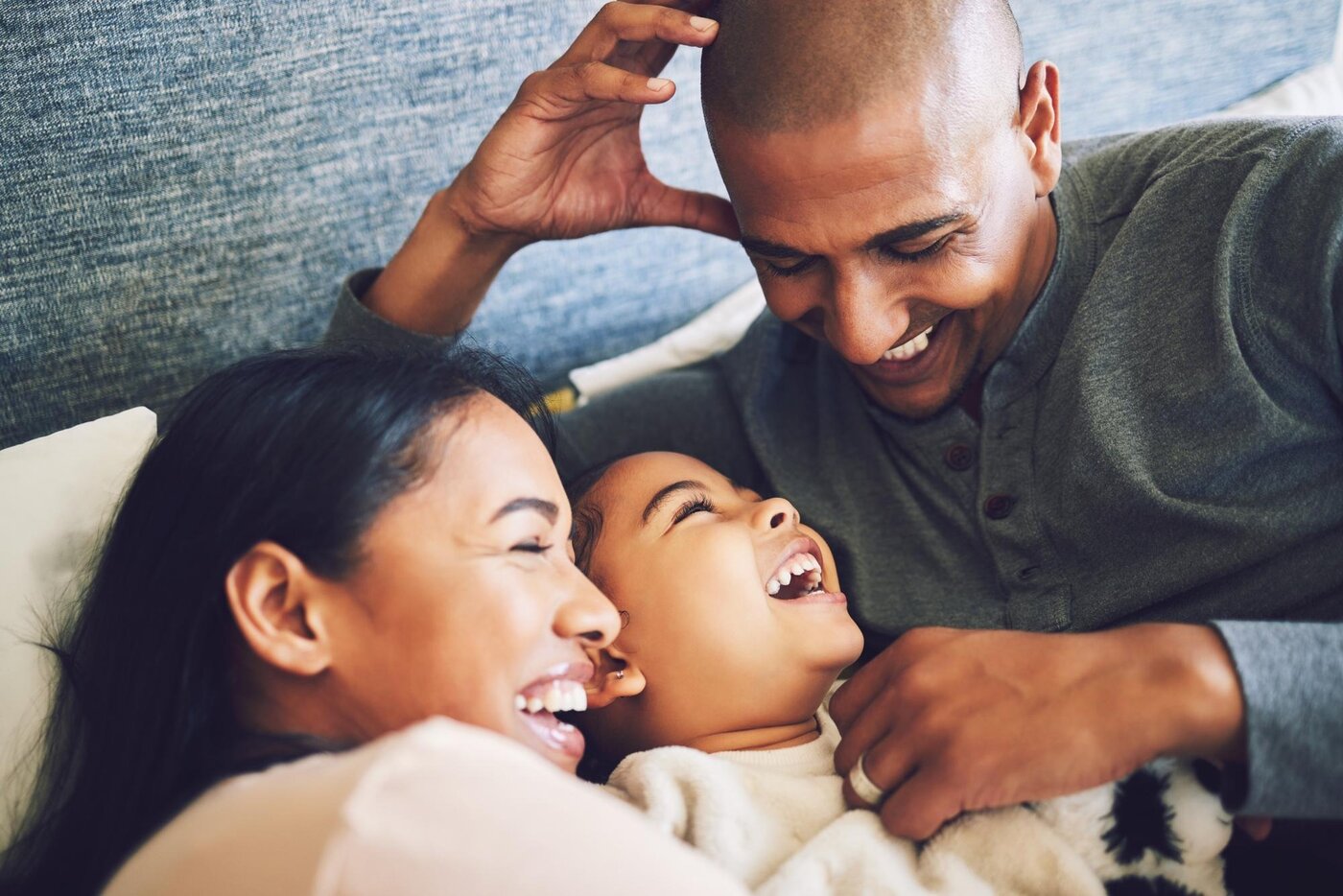 Mum, dad, and their daughter laughing together on the couch at home